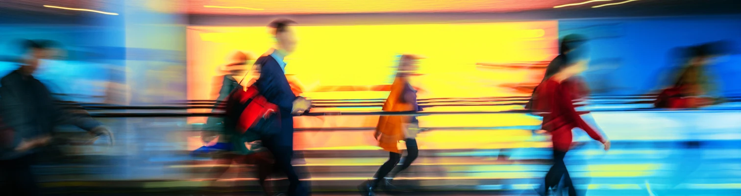 Blurred motion of people walking quickly in front of a colorful blue and yellow background.