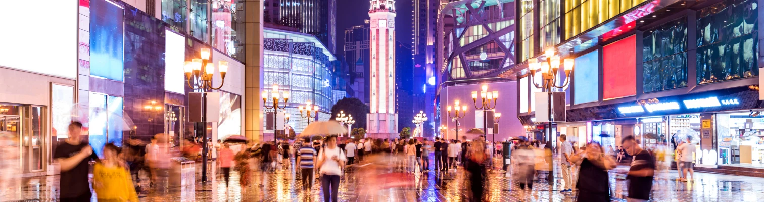 Crowded city street at night with illuminated billboards and a tall clock tower in the background.