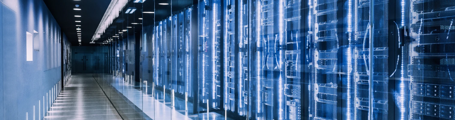 Long hallway of a modern data center with rows of illuminated server racks behind glass panels.