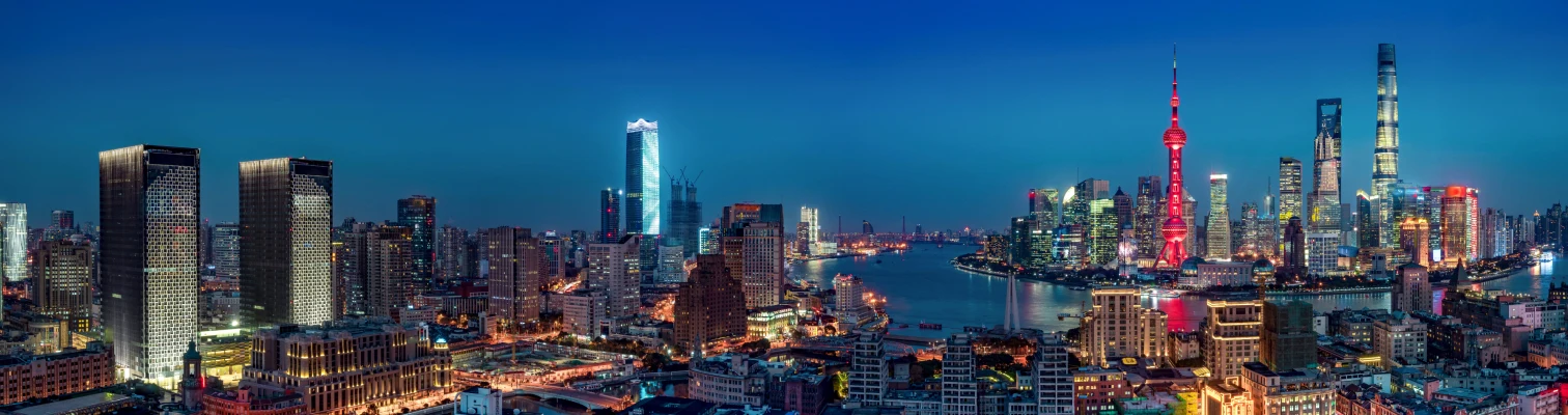 Nighttime panoramic cityscape with illuminated skyscrapers and a river reflecting colorful lights.
