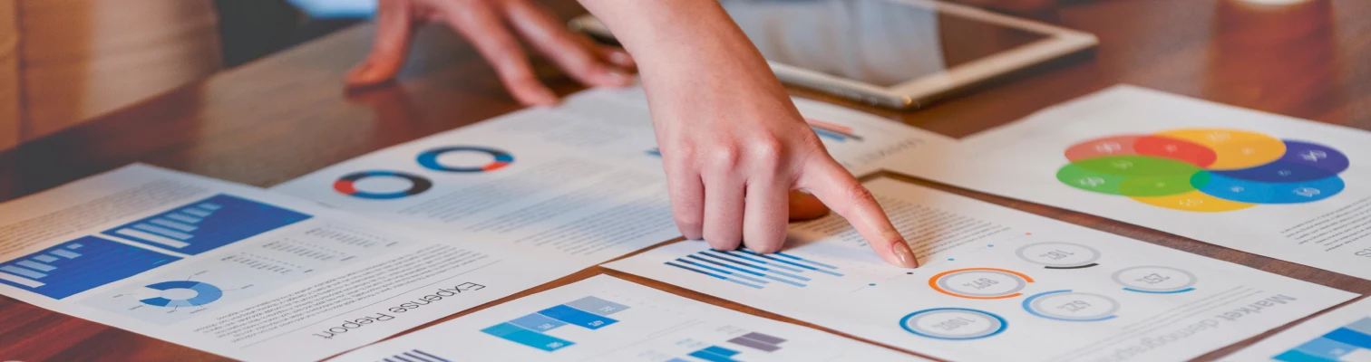 Person pointing at charts and graphs with colorful data visualizations on a wooden table.