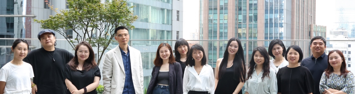 Group of twelve people standing outdoors with city buildings and a tree in the background.